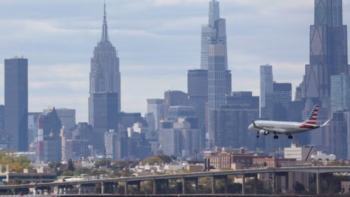 An American Airlines plane descends toward a runway at LaGuardia Airport with the New York City skyline in the background.