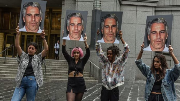 Four protesters hold large posters of Jeffrey Epstein’s face outside a courthouse entrance.