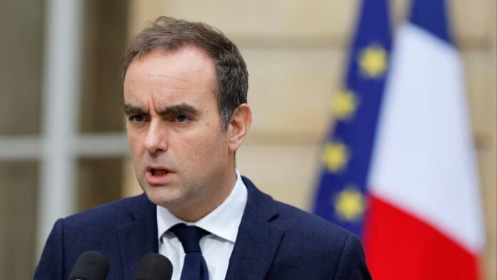 Sébastien Lecornu speaks at microphones, with French and European Union flags blurred in the background.