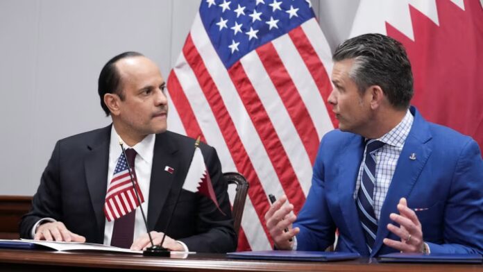 Pete Hegseth and Sheikh Saoud bin Abdulrahman al-Thani seated at a table, talking, with U.S. and Qatari flags behind them.