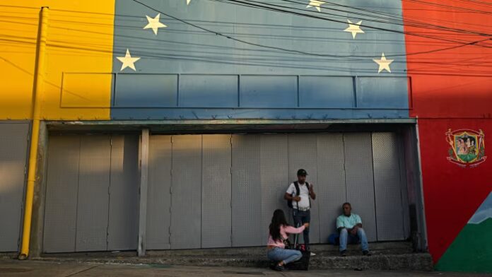 Three people talk in front of a mural painted with the Venezuelan flag's colours and stars in Caracas.