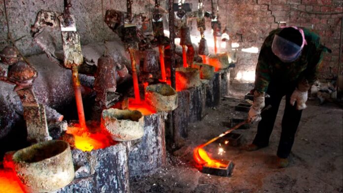 A worker pours molten lanthanum into a mould at the Jinyuan Company smelting workshop, with glowing metal and industrial equipment visible.