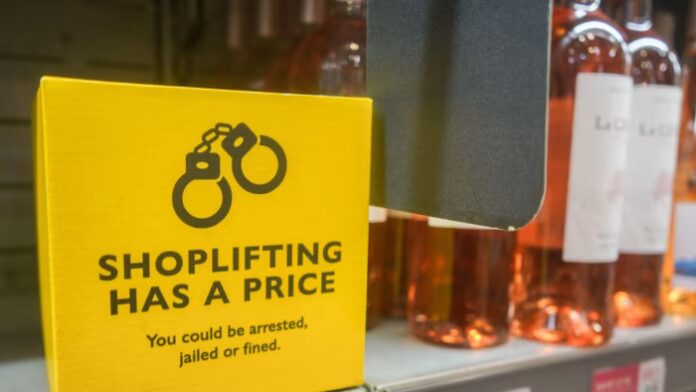 A yellow sign with handcuff icon in a supermarket warns, &quot;Shoplifting has a price. You could be arrested, jailed or fined,&quot; near bottles of wine.