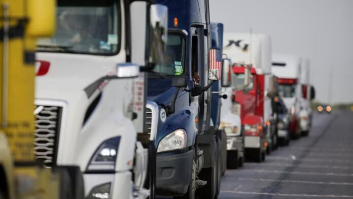 Semi-trucks line up in a long queue on a road, waiting for border customs control to cross into the U.S.